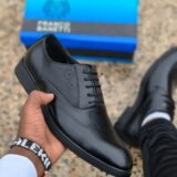 A hand holding a pair of black loafers, showcasing the brand's signature style and quality.