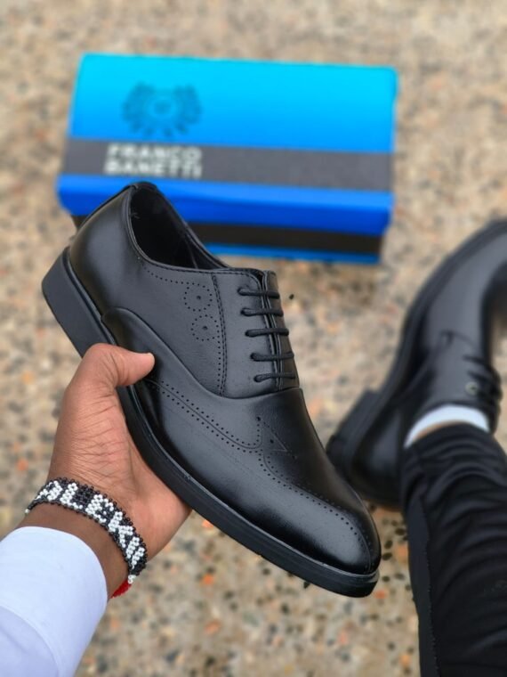 A hand holding a pair of black loafers, showcasing the brand's signature style and quality.