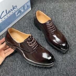 A hand holding a pair of Clarks shoes, showcasing the product's polished finish and classic design.