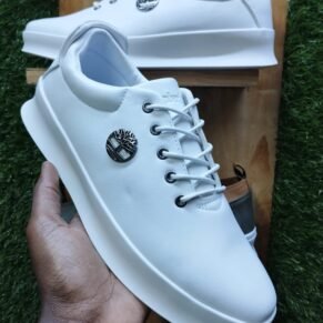 A hand holding a pair of white Timberland sneakers with a tree logo on the side, showcasing the brand's signature design and quality.