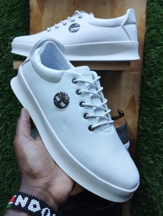 A hand holding a pair of white Timberland sneakers with a tree logo on the side, showcasing the brand's signature design and quality.